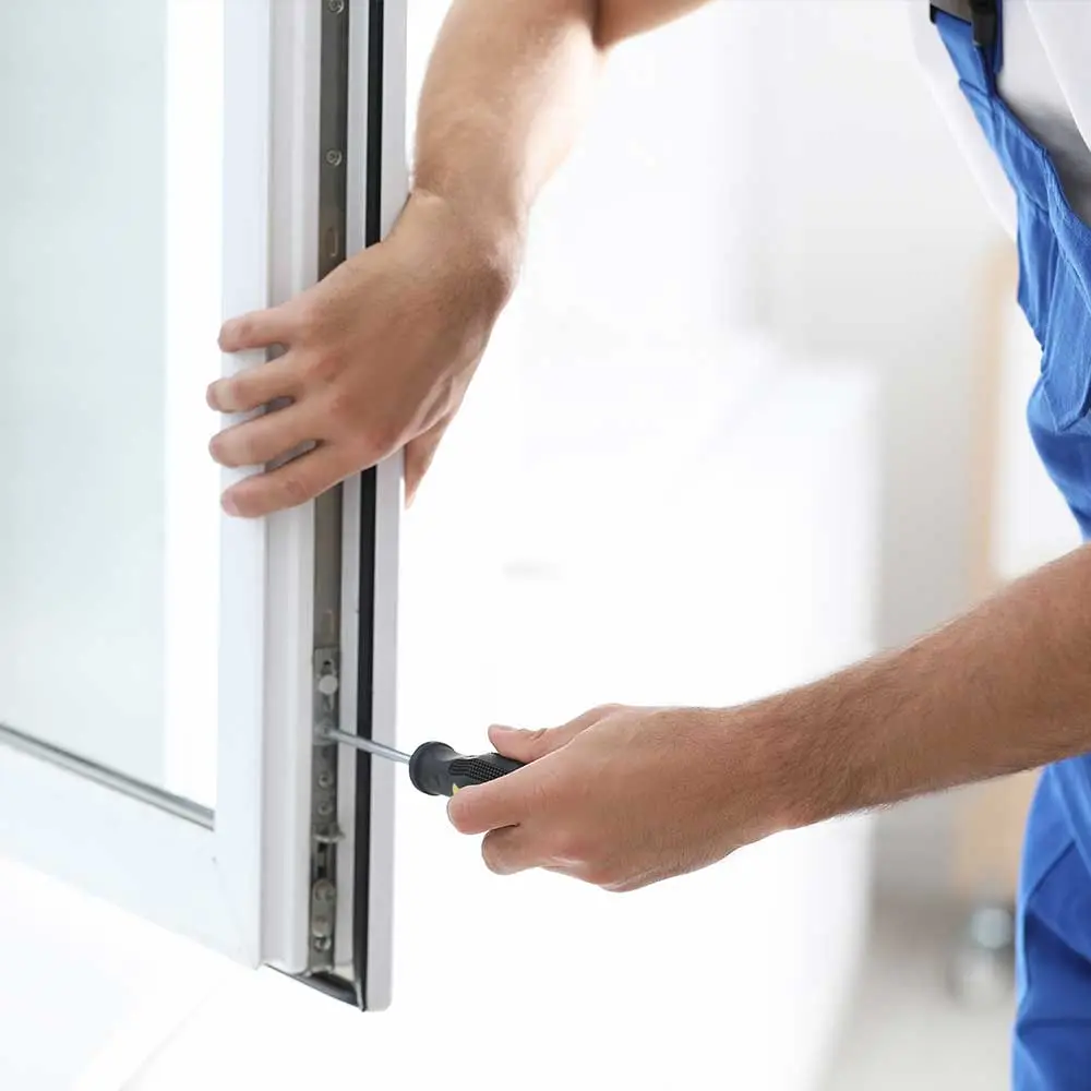 Handwerker justiert Fensterbeschlag mit Schraubenzieher – sorgfältige Wartungsarbeit