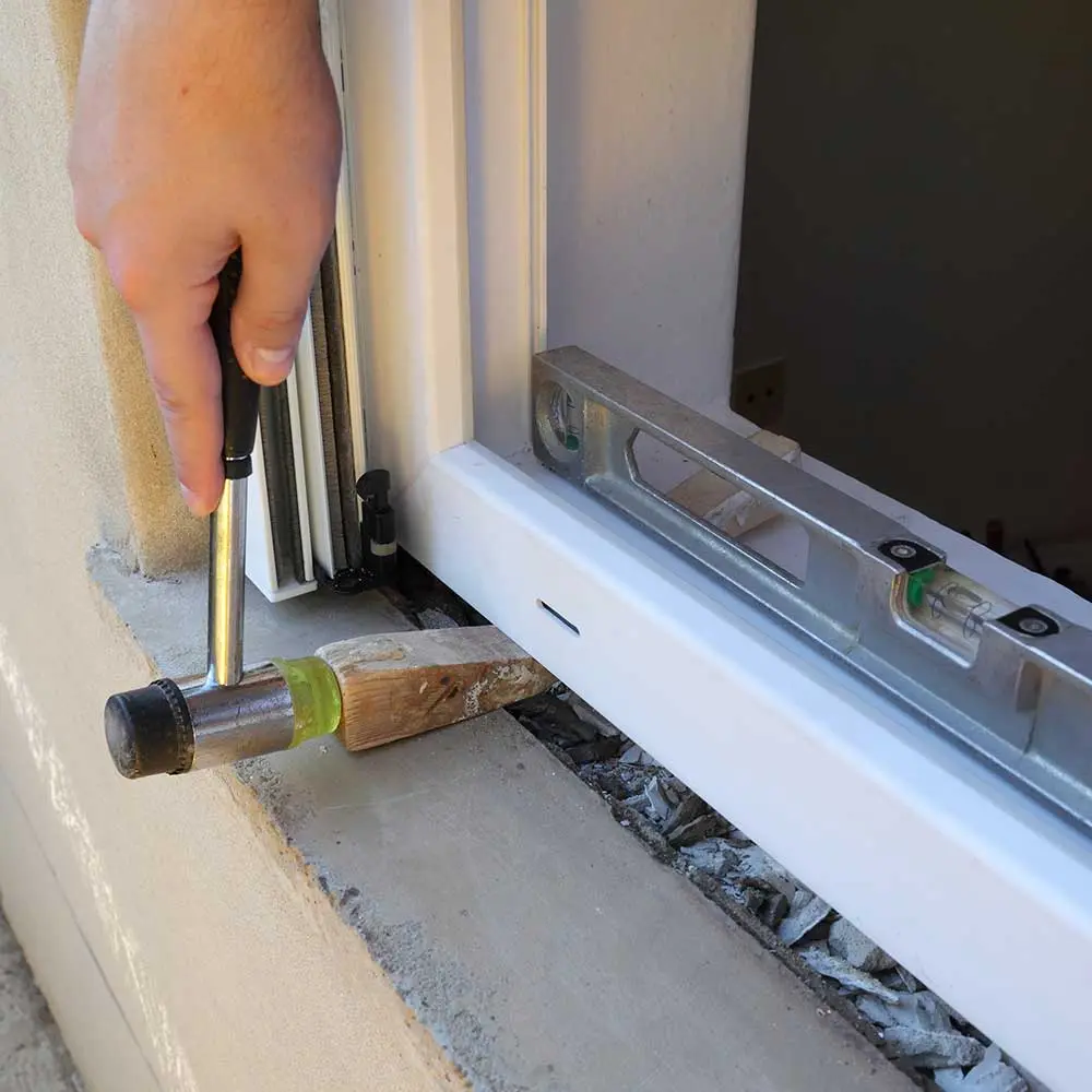 Fenstermontage durch Handwerker mit Wasserwaage und Hammer – präzise Ausrichtung