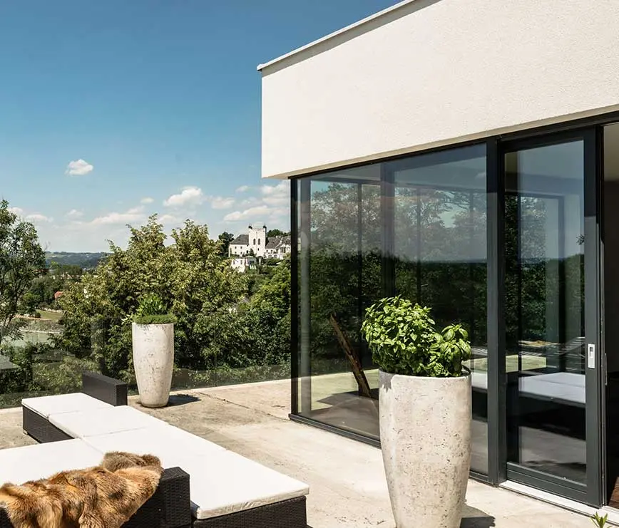 Terrasse mit modernen Ganzglas-Schiebeelementen und Blick ins Grüne.
