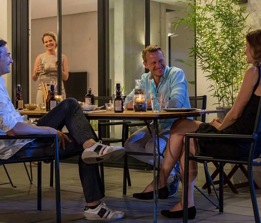 Freunde sitzen abends geschützt vor Insekten auf der Terrasse und genießen Getränke.