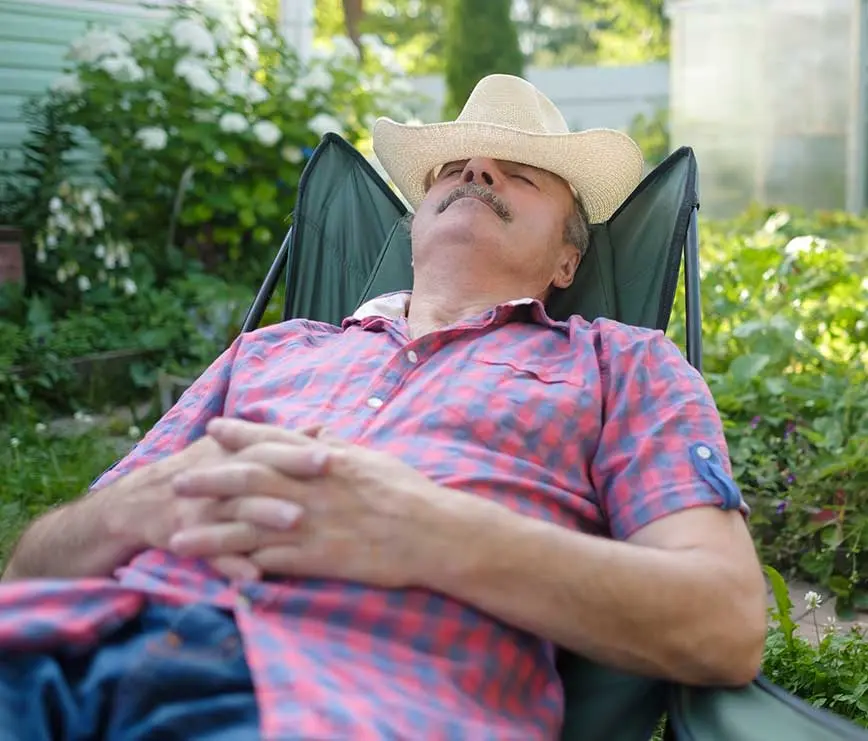 Mann mit Hut schläft entspannt im Gartenstuhl